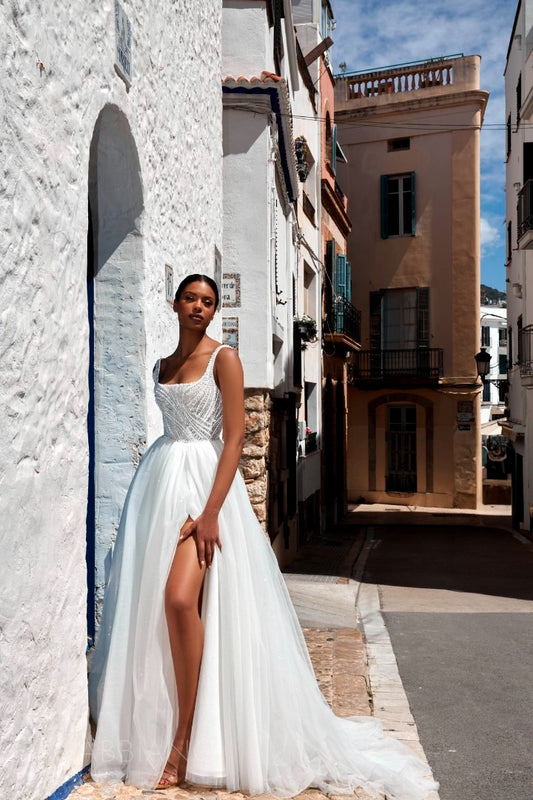 Bride wearing Danis gown with slit skirt standing against whitewashed stone wall