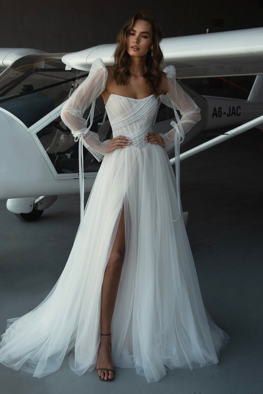 Kris by Natalia Romanova tulle A-line wedding dress with pearl-draped strapless bodice, detachable sheer puff sleeves, and thigh-high slit.